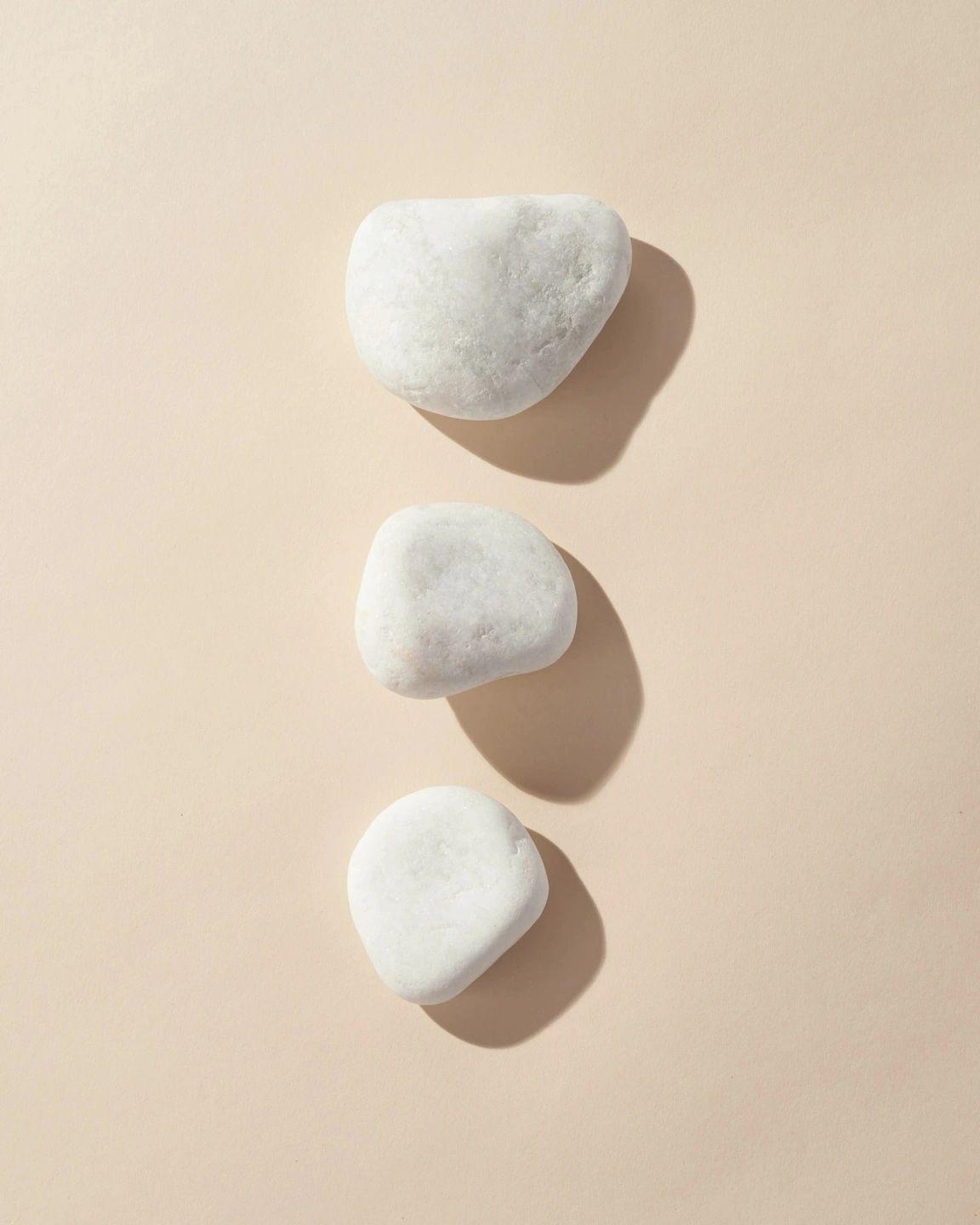 Three smooth white stones stacked in a line on a soft beige background