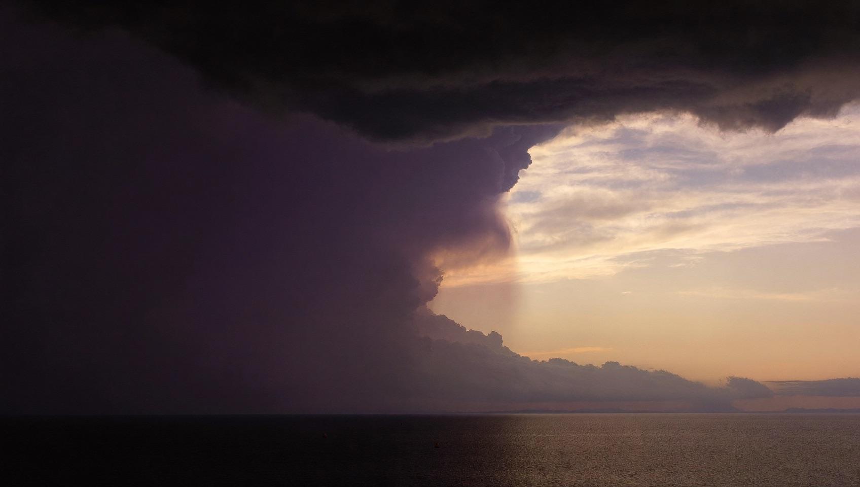 Dark storm clouds over calm water giving way to golden dawn light